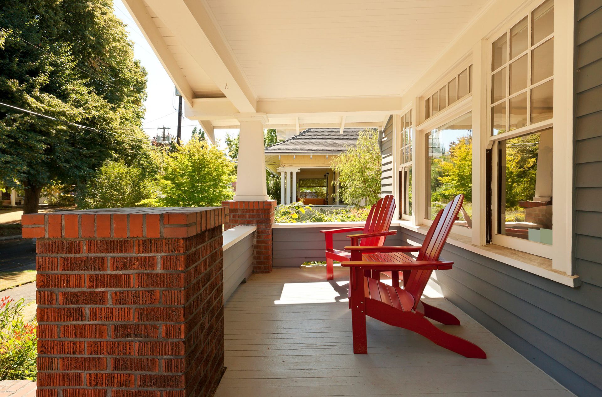 A porch with two red chairs and a brick wall.