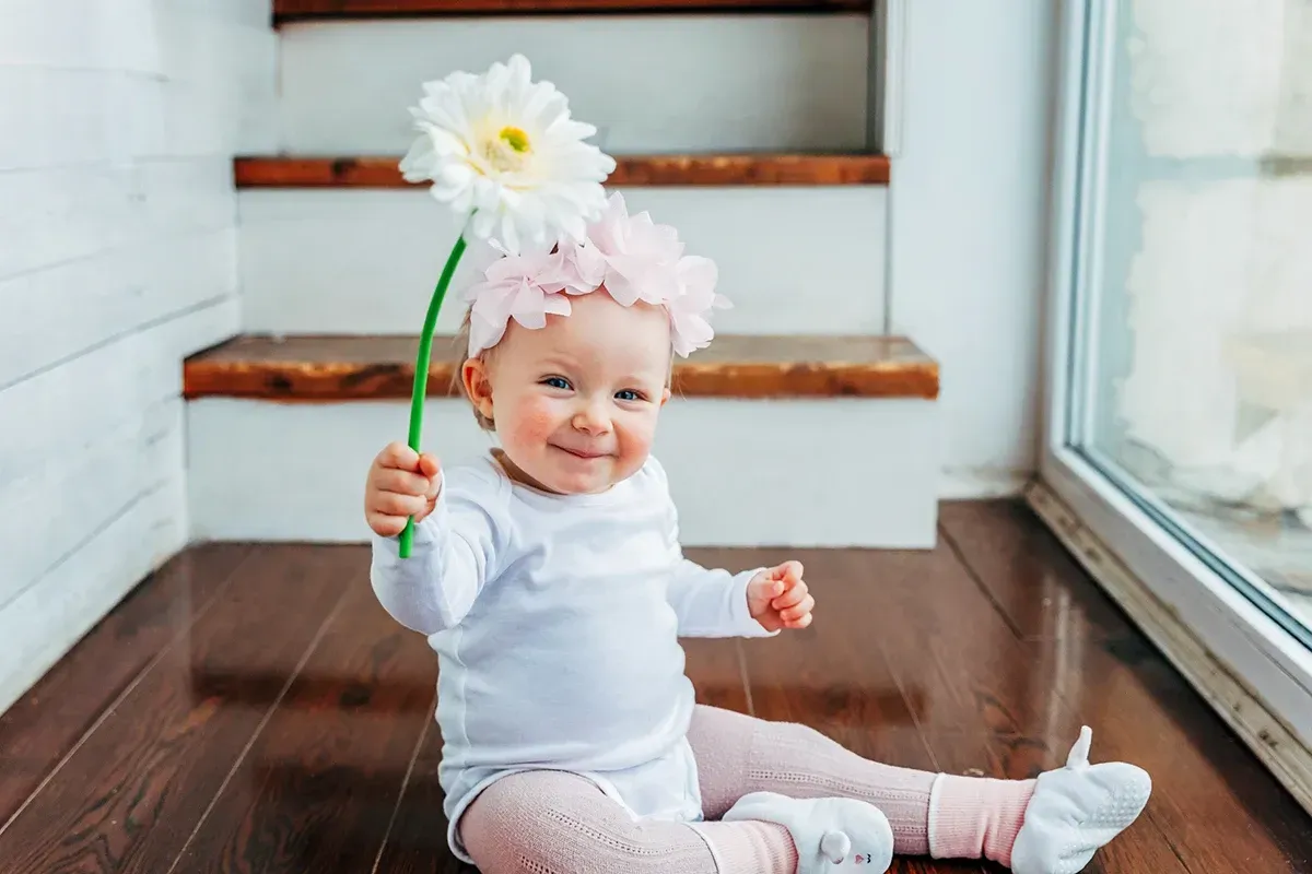 Smiling baby holding a flower sitting on low VOC flooring.