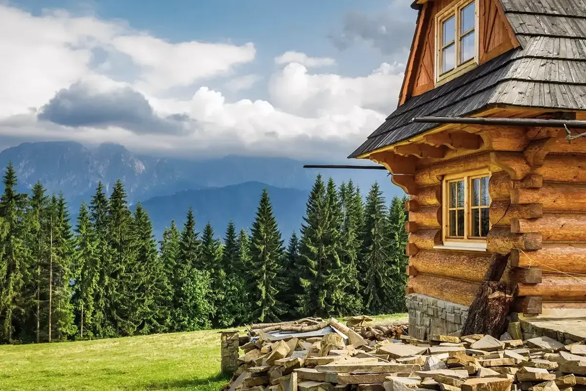 Log cabin on a mountain top surrounded by a forest with rain clouds in the distance.