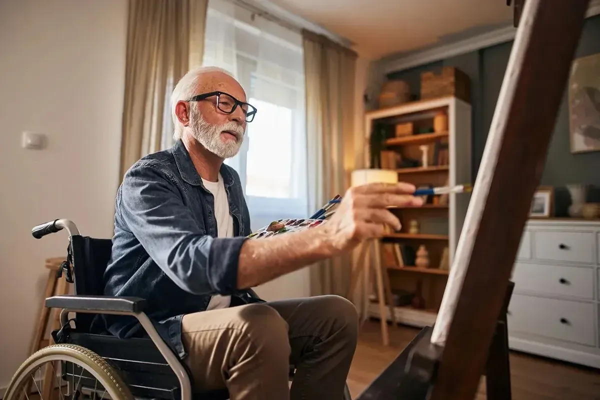 Man in a wheelchair painting at home.