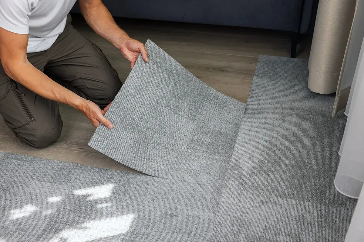 Man installing carpet tiles, another cheap flooring option.