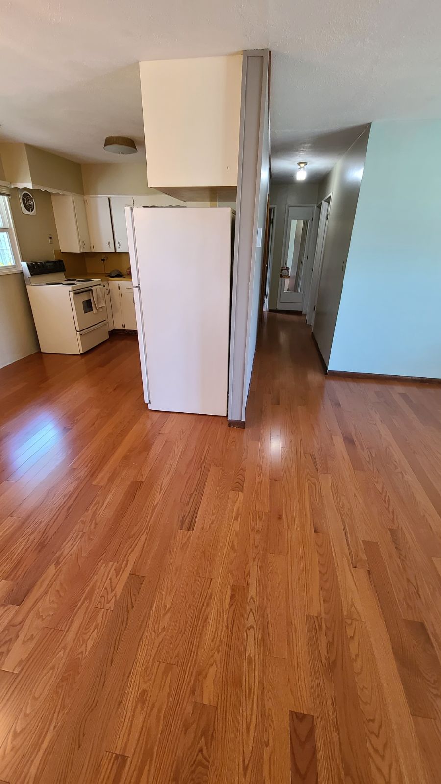 An empty kitchen with hardwood floors and a refrigerator.