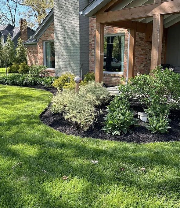 A house with a brick exterior and well-manicured landscaping. Green grass and mulch surround the foundation.