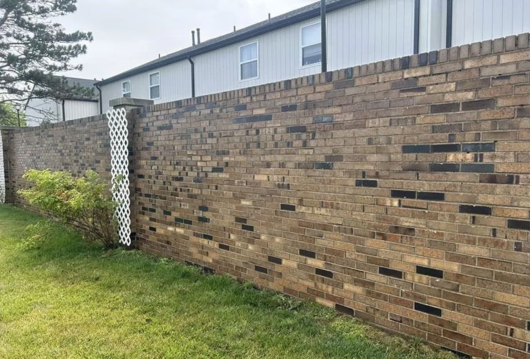 Brick wall with green grass in front and a white building in the background.