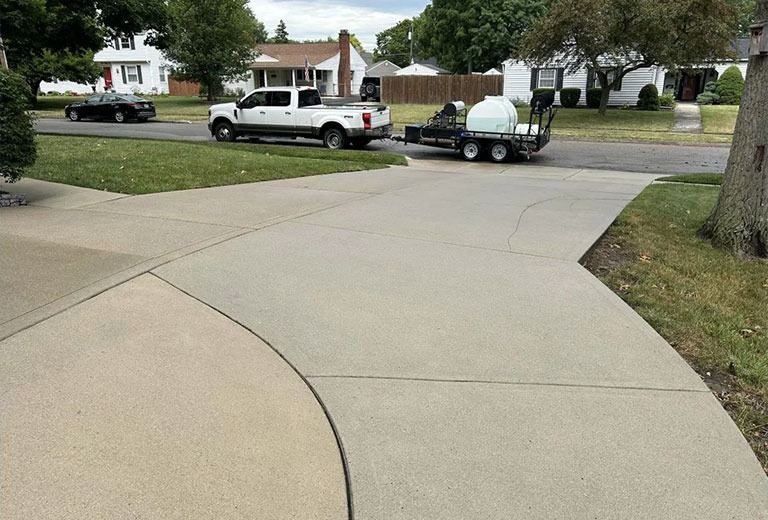 A white truck towing a trailer with equipment on a driveway in a residential neighborhood.