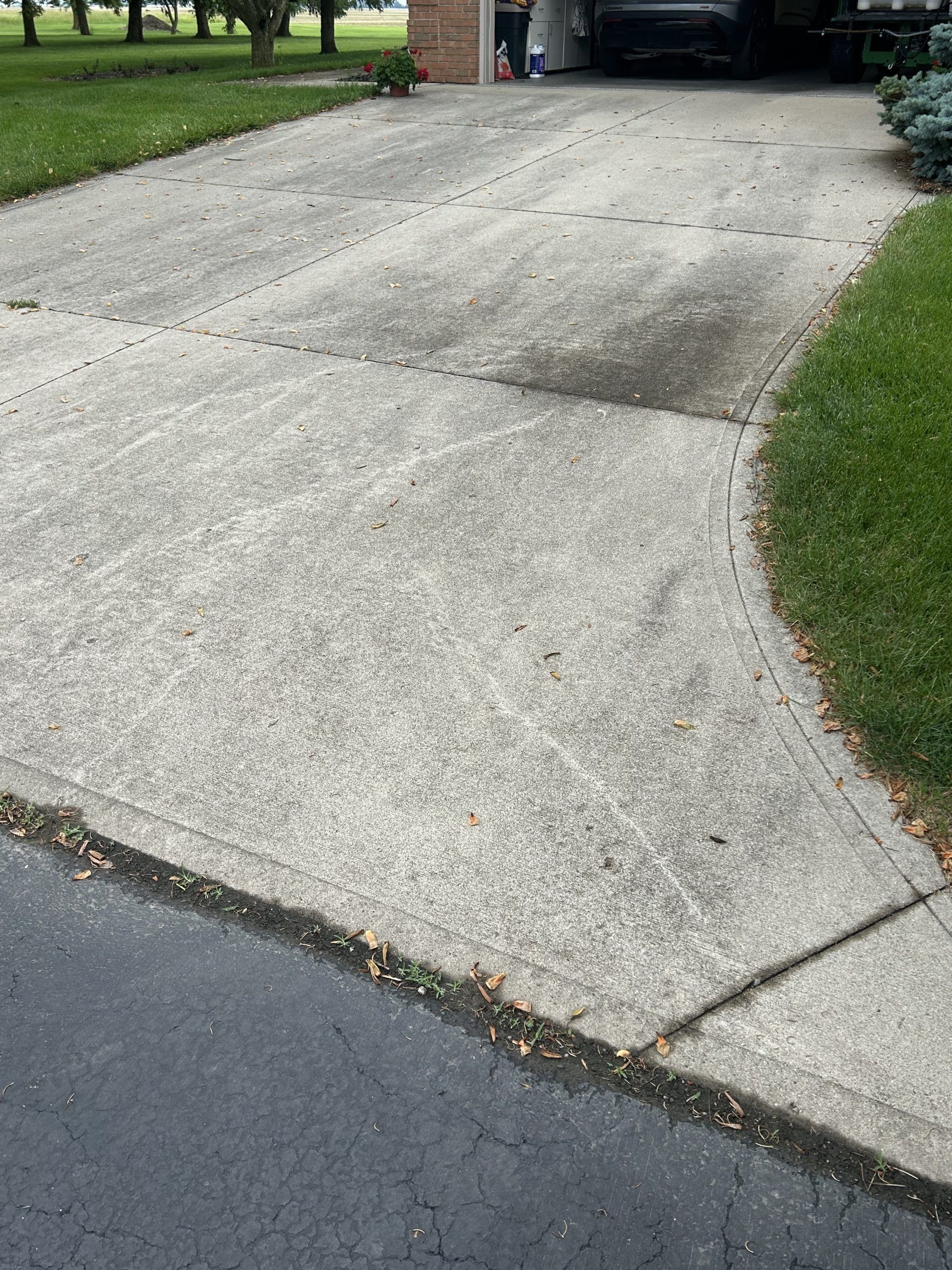 Concrete driveway curving into grass. Shows faded stains and a paved road edge.