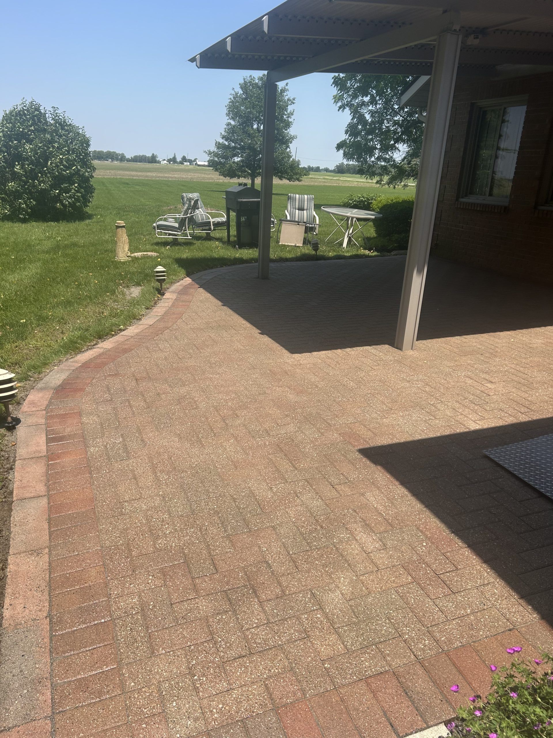 Brick patio with a covered area, a pathway, and green lawn in a sunny outdoor setting.