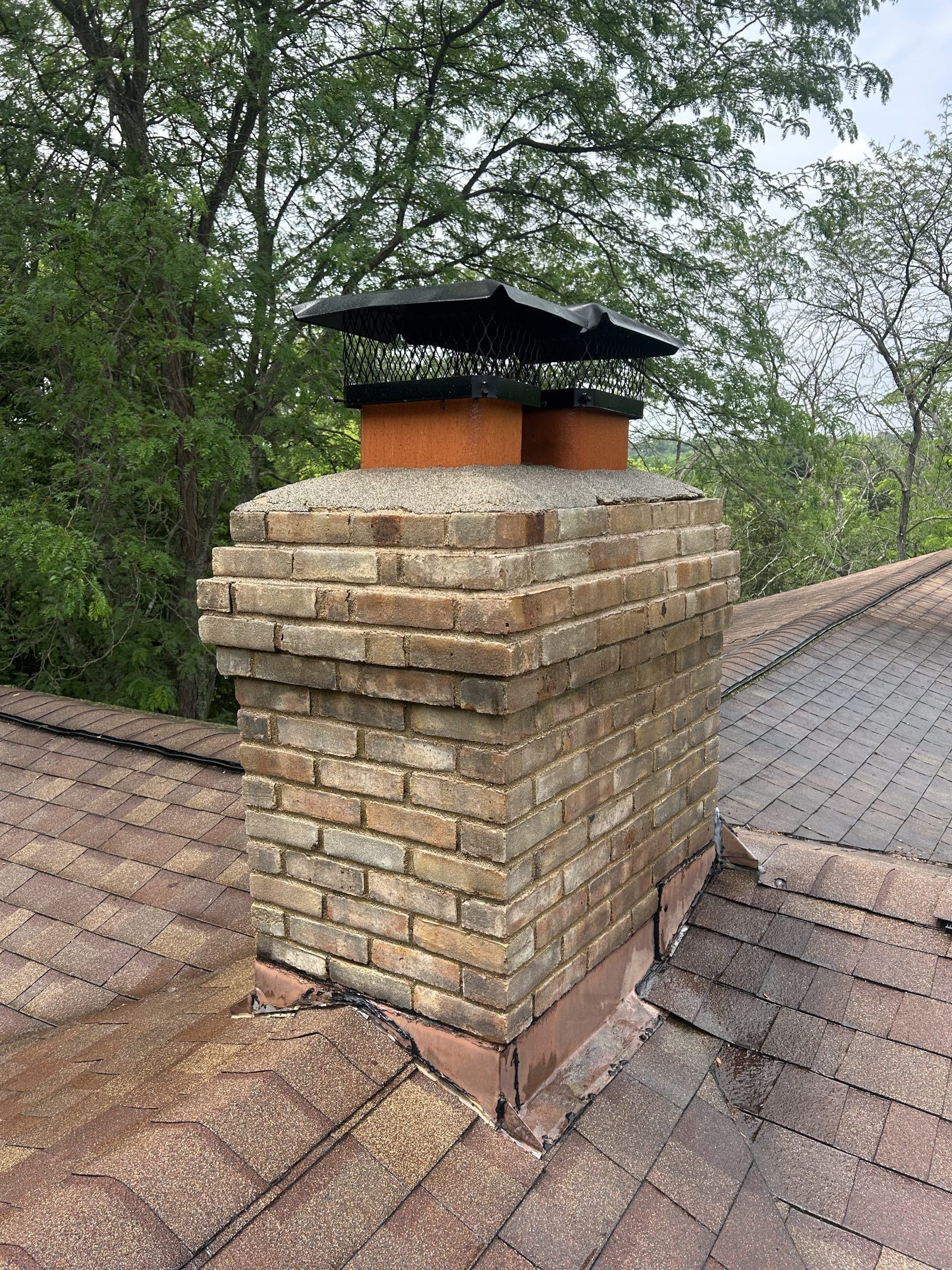 Brick chimney on a shingled roof, with a black chimney cap.