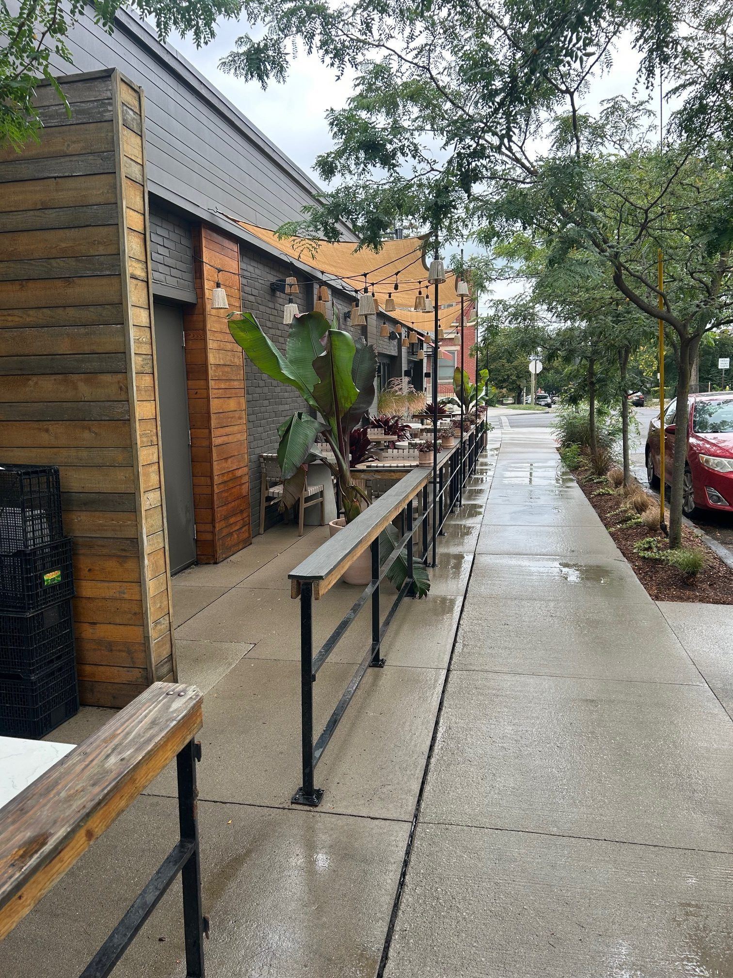 Outdoor restaurant seating along a sidewalk, with wooden accents, and metal railings.