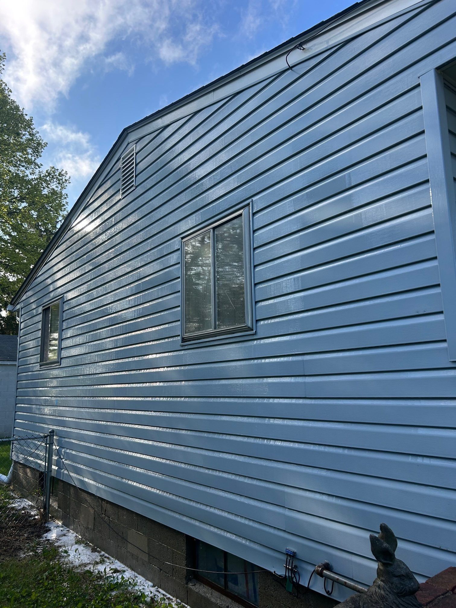 Side view of a light blue house with siding, windows, and a cloudy sky.