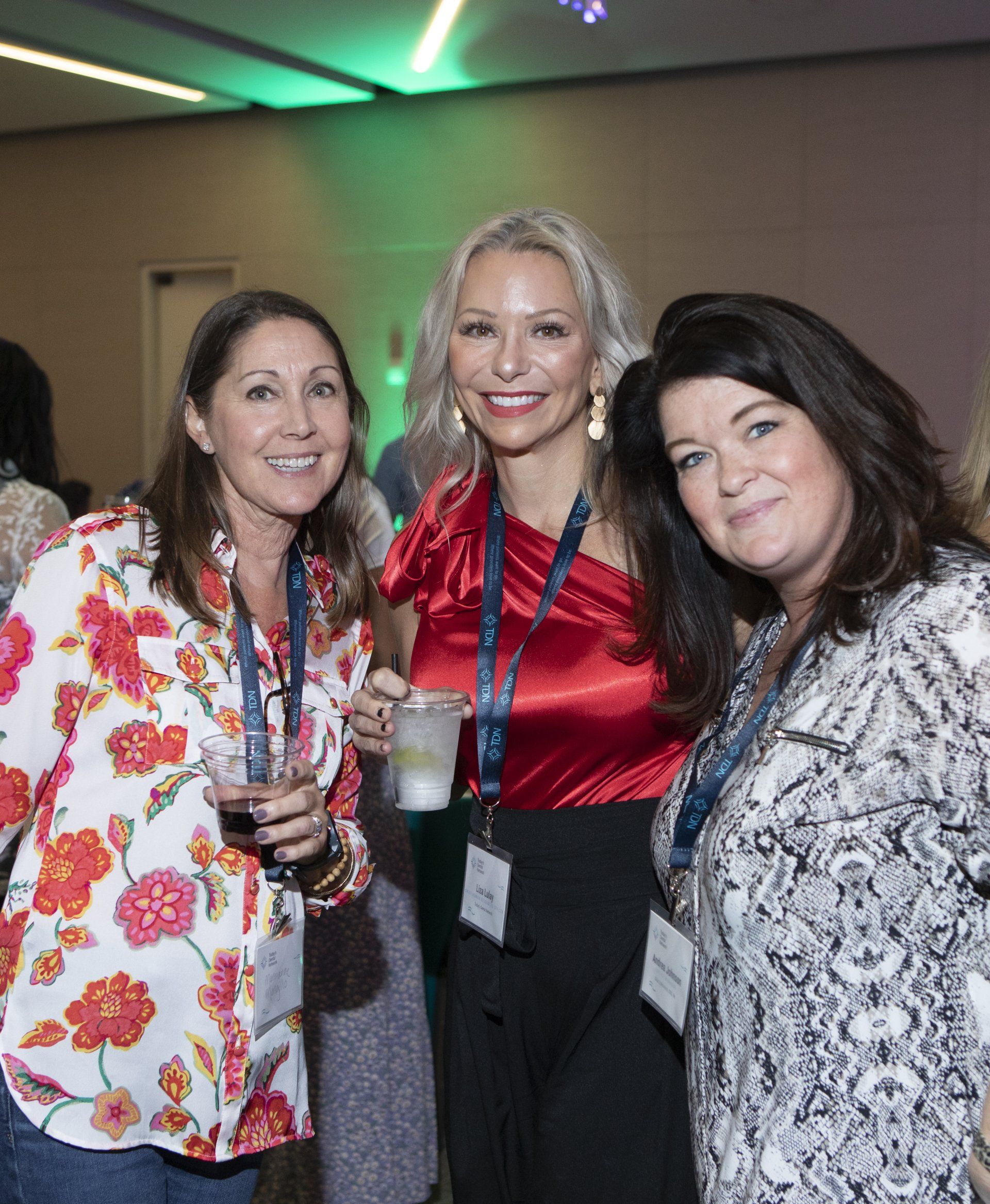 Three women are posing for a picture at a party while holding drinks.