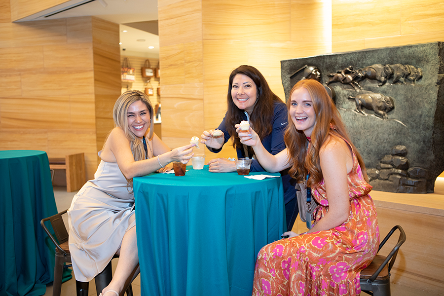Three women are sitting at a table holding cups of coffee.