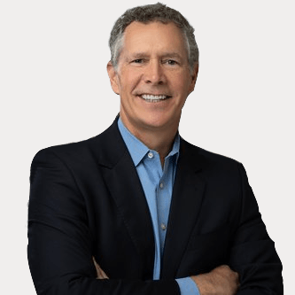 A man in a suit and blue shirt is smiling with his arms crossed.