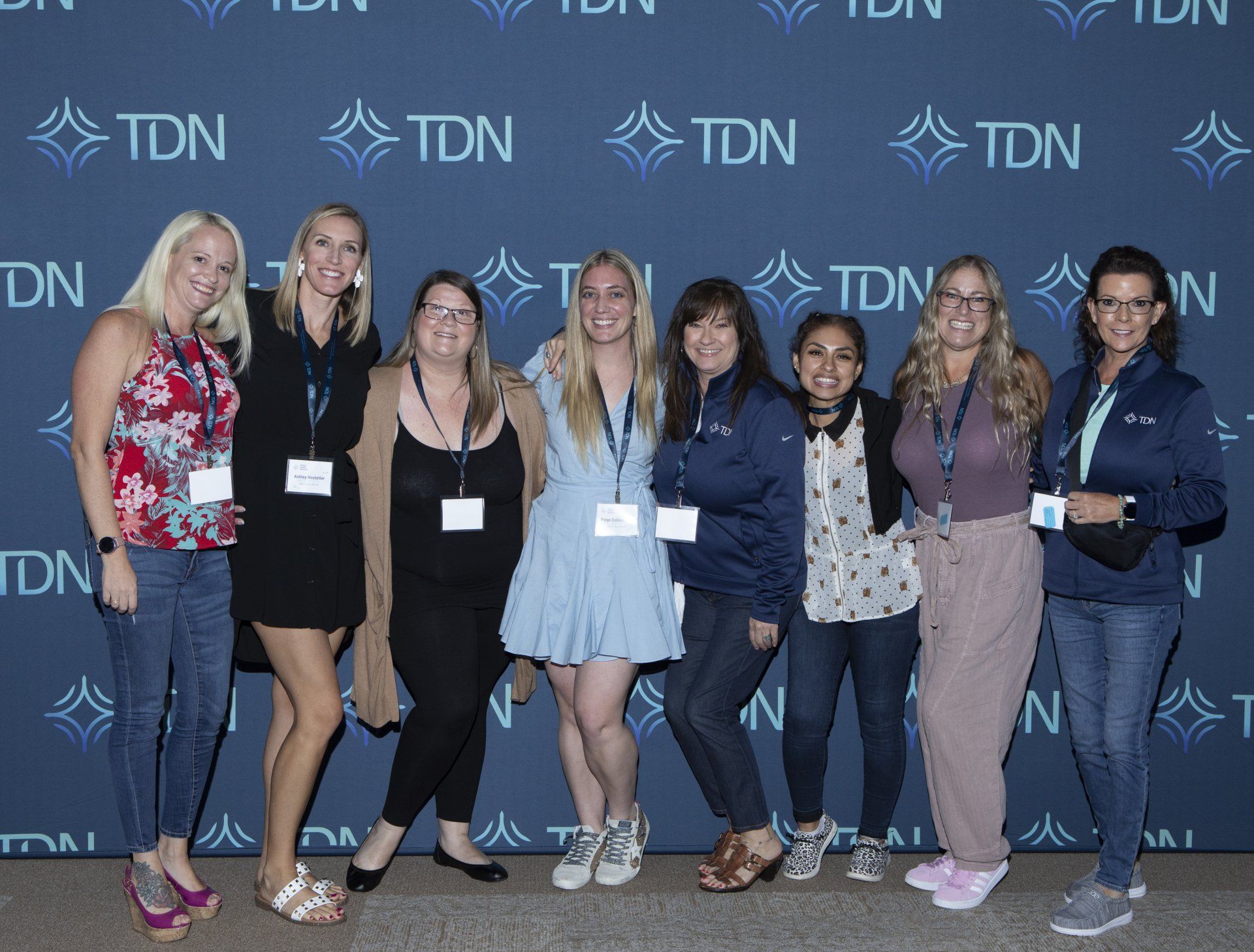 A group of women are posing for a picture in front of a wall that says tdn