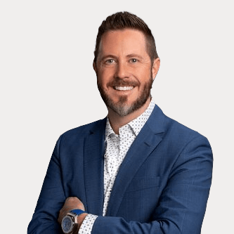 A man in a blue suit and white shirt is smiling with his arms crossed.