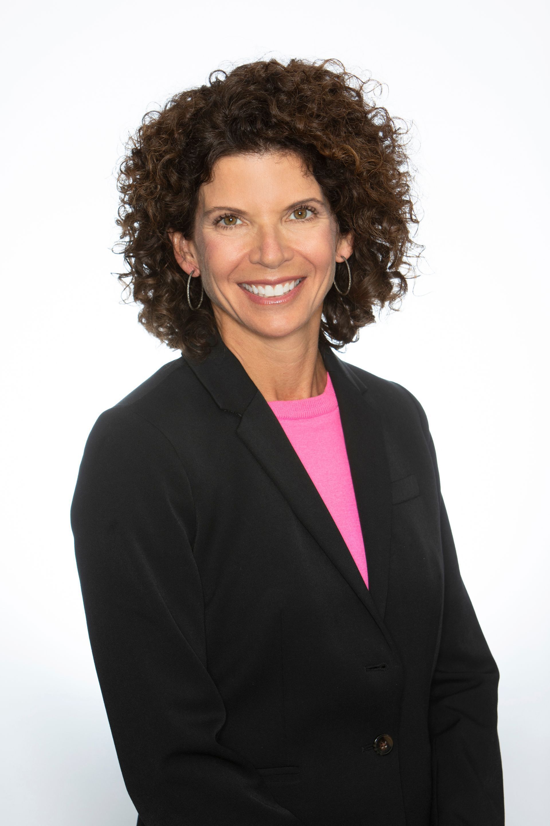 A woman with curly hair is wearing a black jacket and a pink shirt.