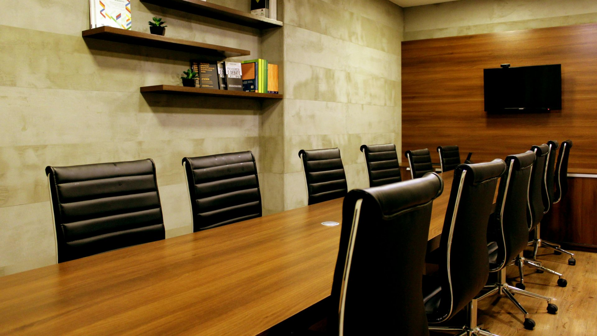 Conference room with long wooden table, black leather chairs, and TV.