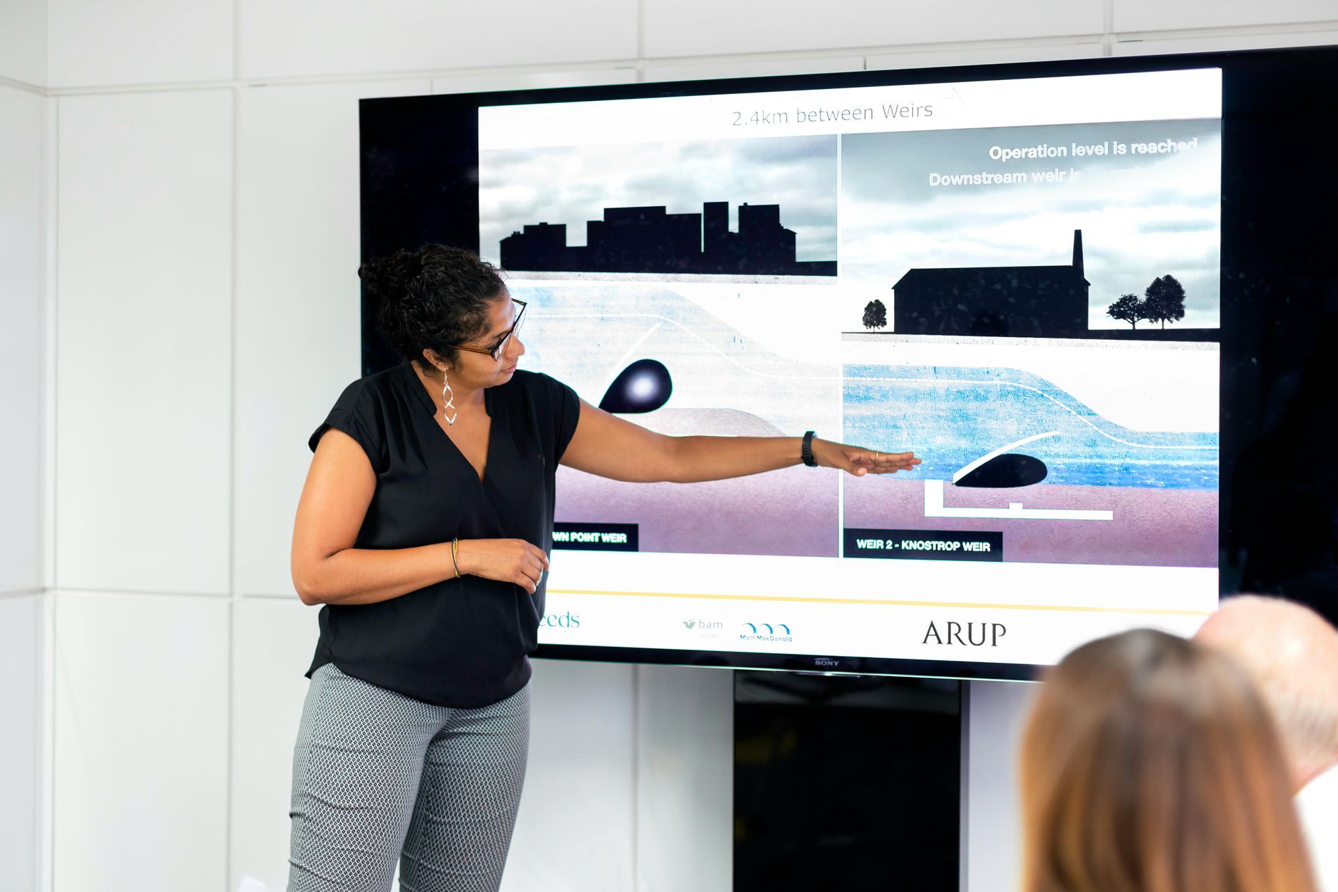 Woman pointing at a diagram on a screen, presenting to a seated audience.