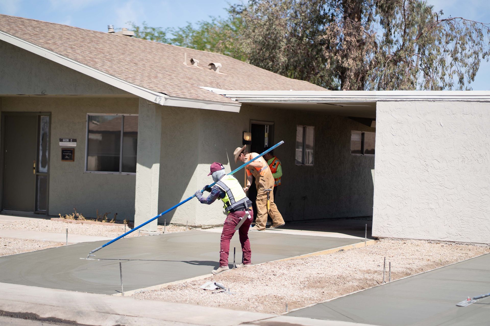 Workers smoothing wet concrete sidewalk in front of a house.
