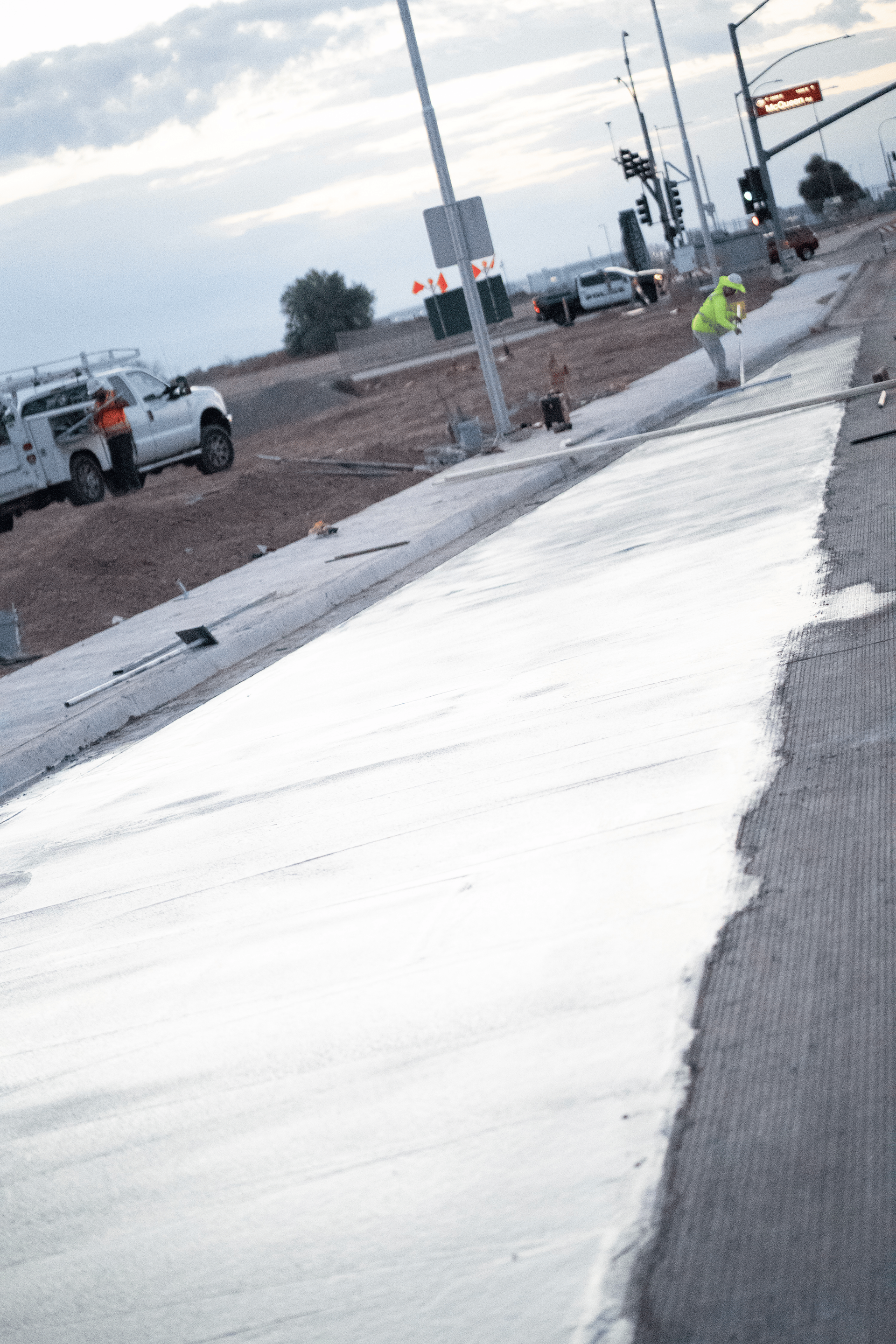 Road construction scene with workers, truck, and a police car; white paint applied on the side of the road.