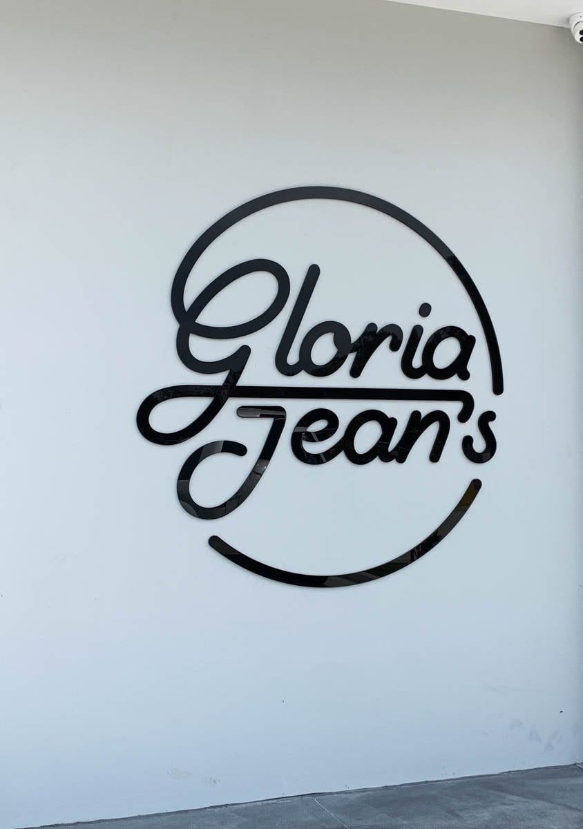 The Logo For Gloria Jeans Is Painted On A White Wall — Solis Signs in Toukley, NSW