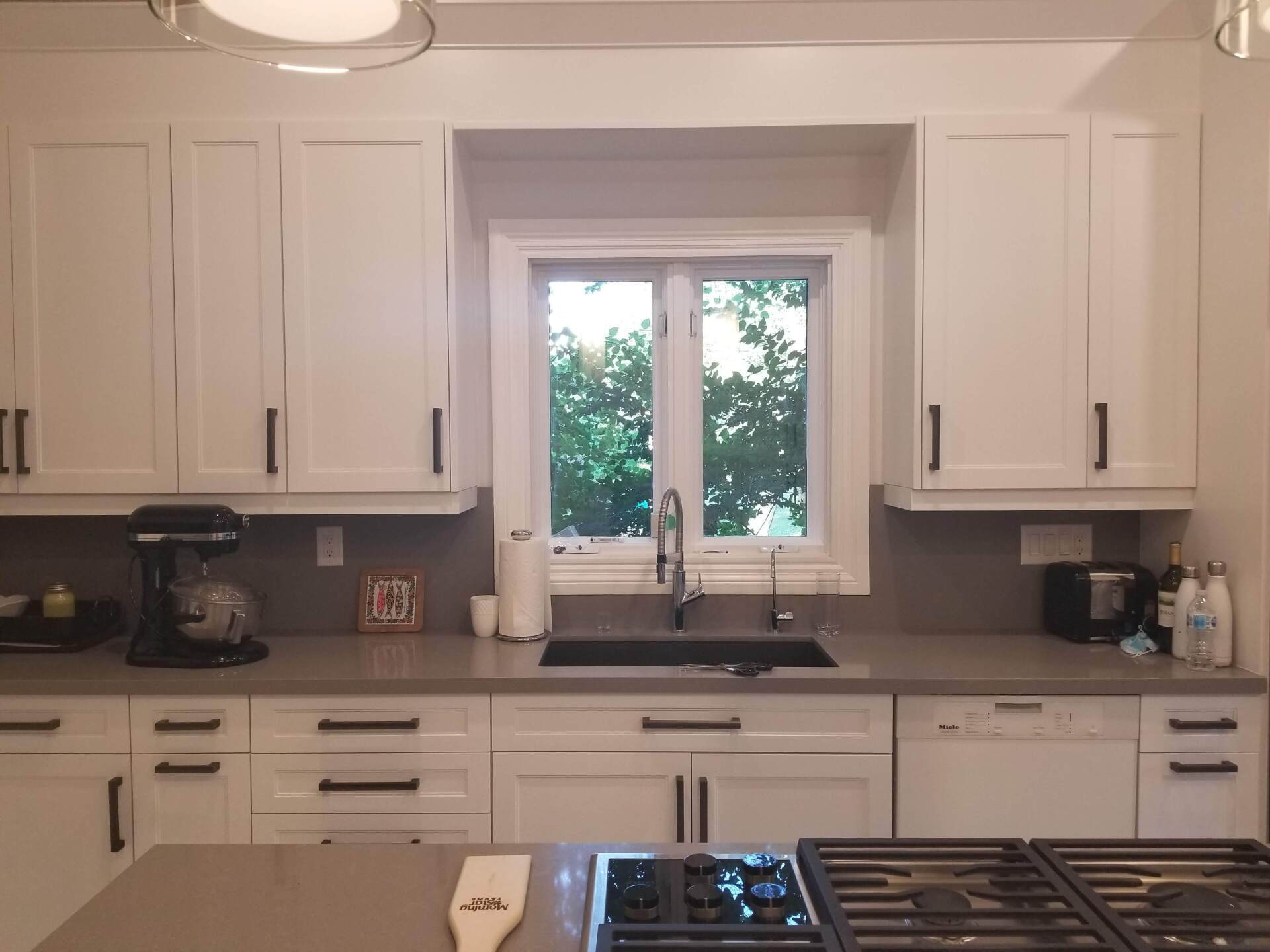 A kitchen with white cabinets , a sink , a stove , and a window.