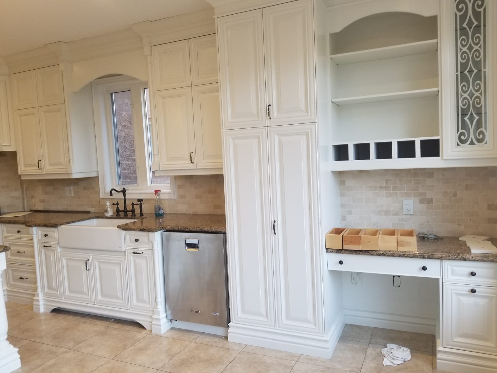 A kitchen with white cabinets , a sink , a dishwasher and a desk.