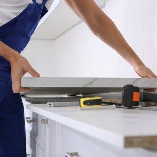 A man in blue overalls is working on a kitchen counter.