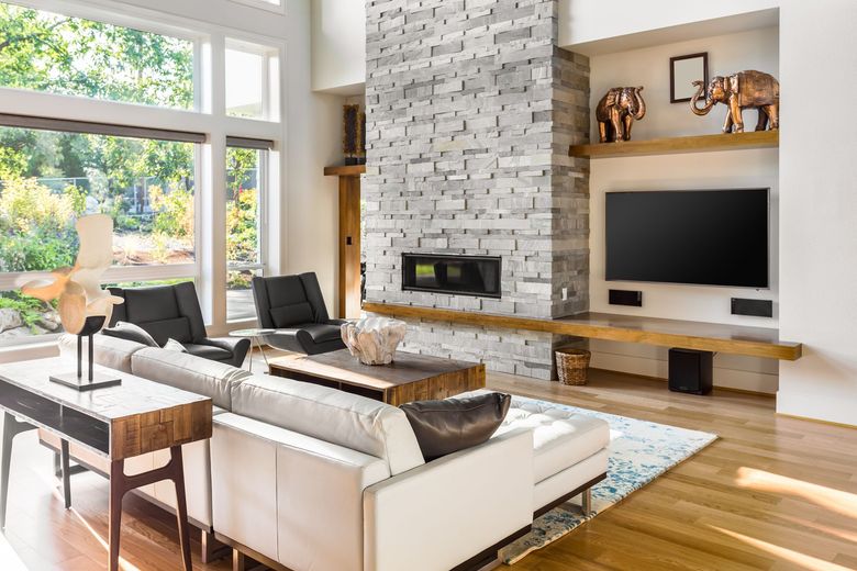 Modern living room with stone fireplace, large windows, light-colored sofa, and wooden accents.