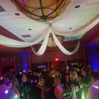 Crowded dance floor in a dim banquet hall with colorful lights and draped ceiling fabric