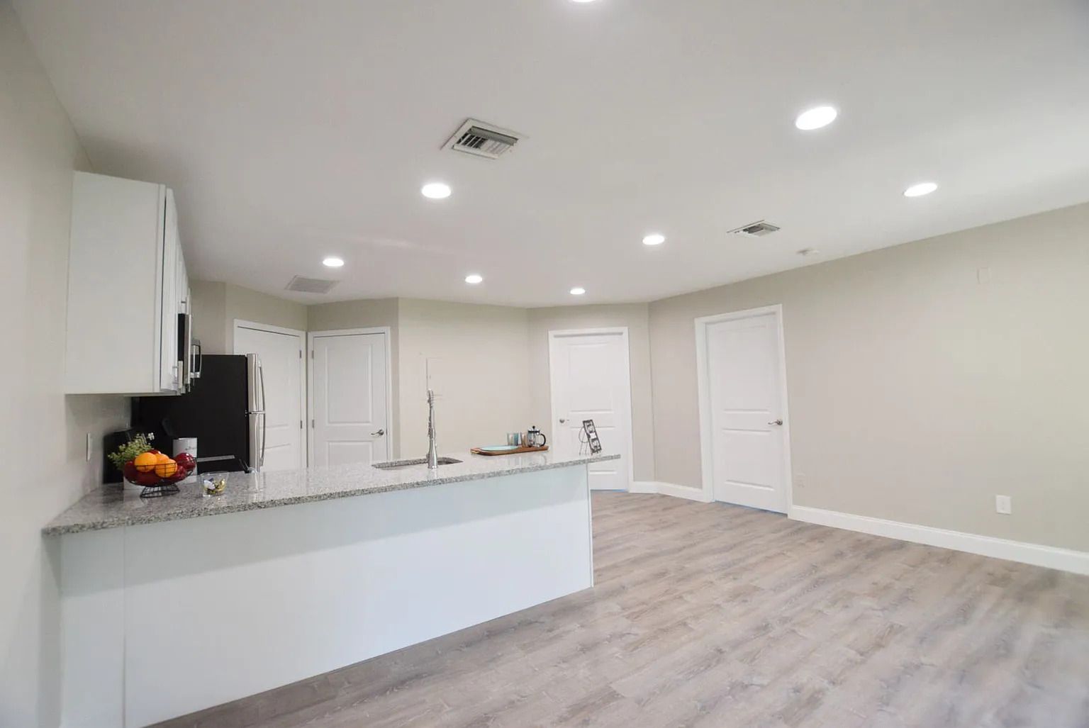 A living room with hardwood floors and a kitchen in the background.
