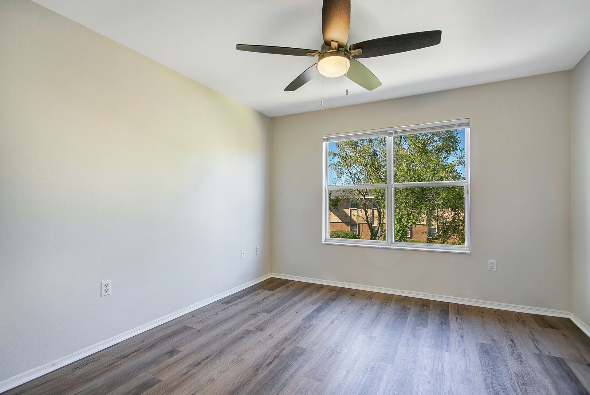 An empty room with a ceiling fan and two windows.
