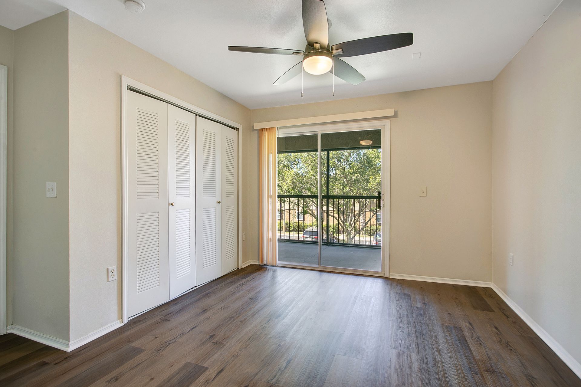 An empty room with a ceiling fan and sliding glass doors leading to a balcony.
