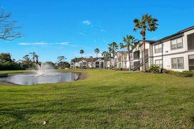 There is a fountain in front of a building next to a lake.