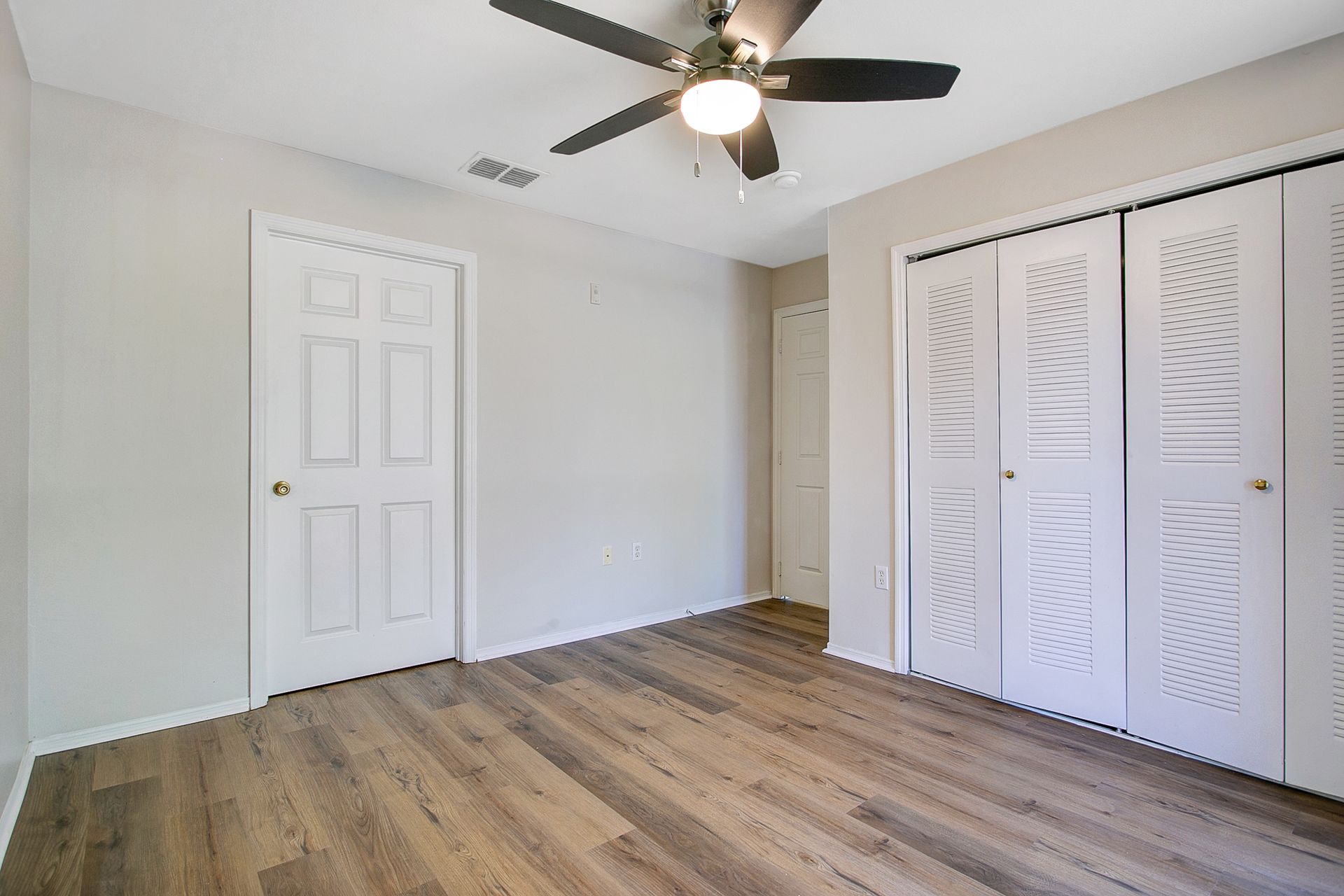 An empty bedroom with hardwood floors and a ceiling fan.