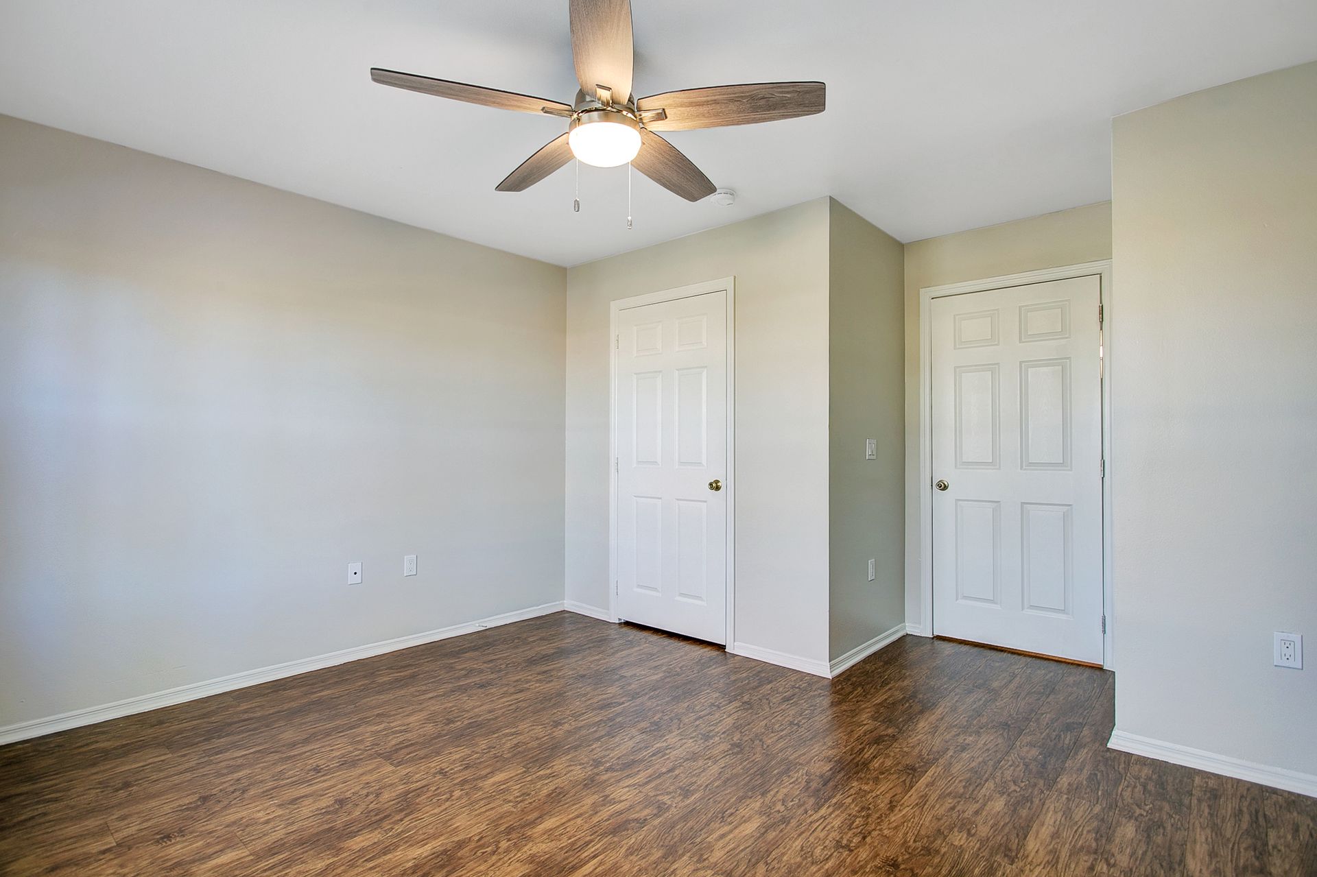 An empty bedroom with hardwood floors and a ceiling fan.