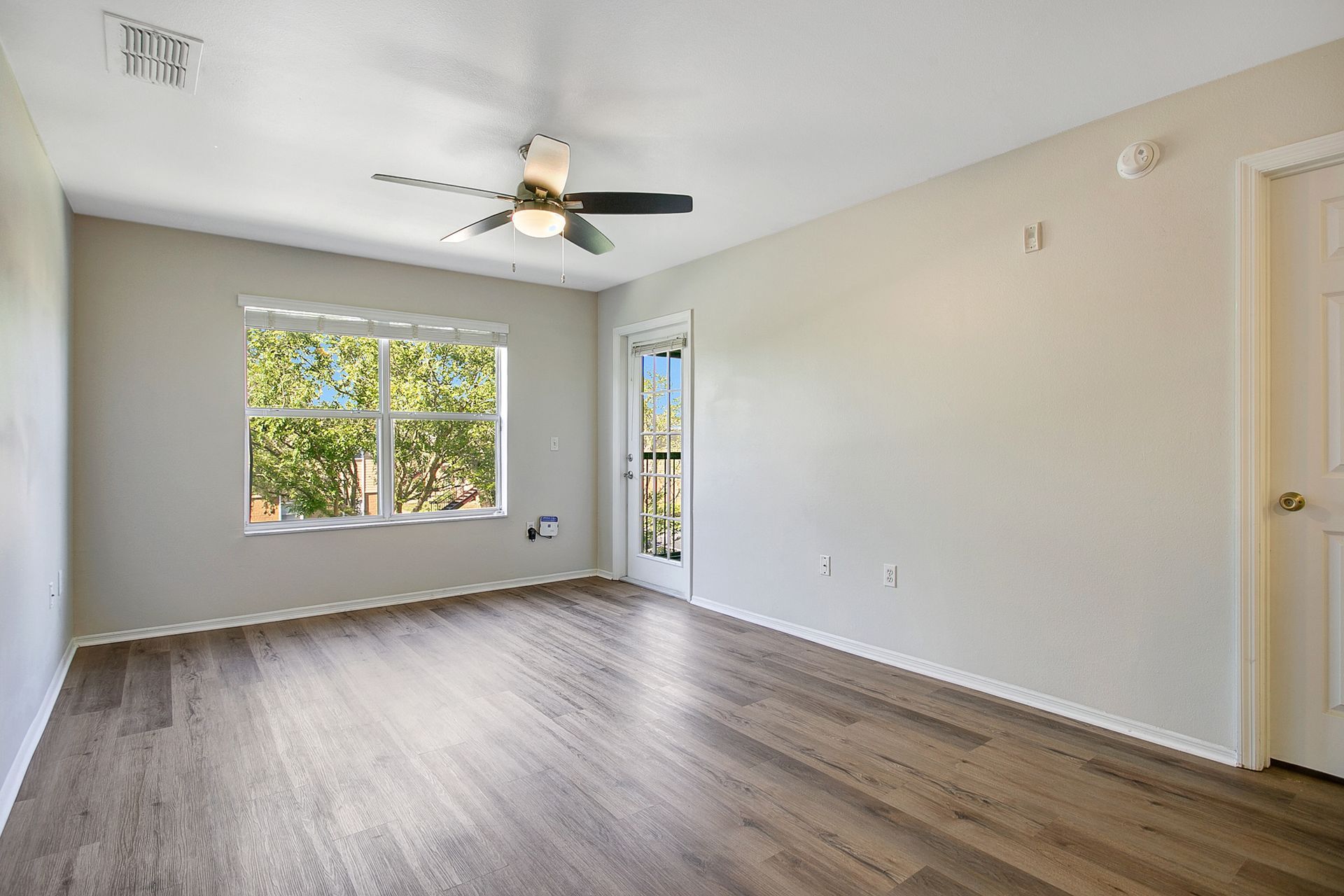 An empty living room with hardwood floors and a ceiling fan.