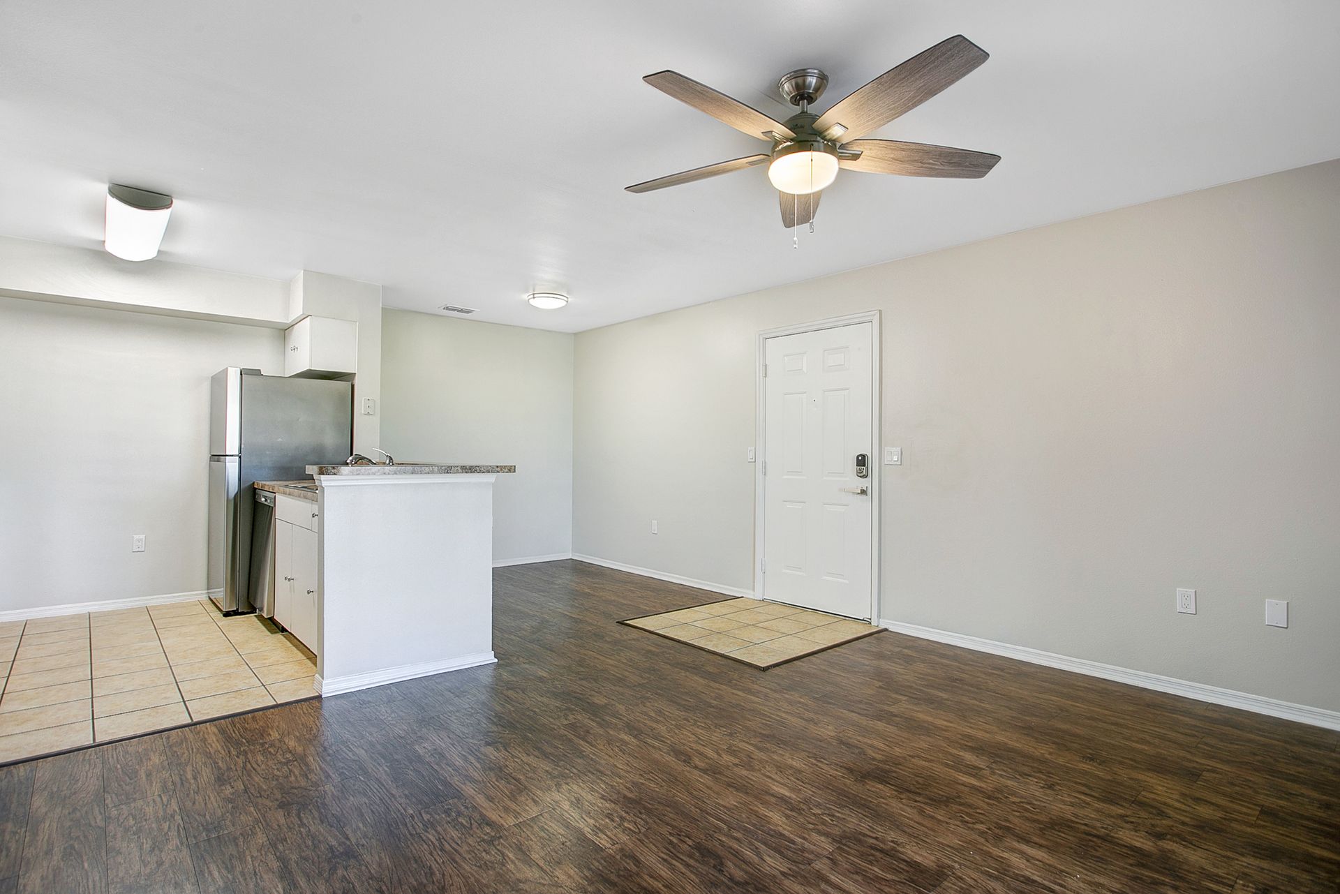 An empty living room with a ceiling fan and a refrigerator.