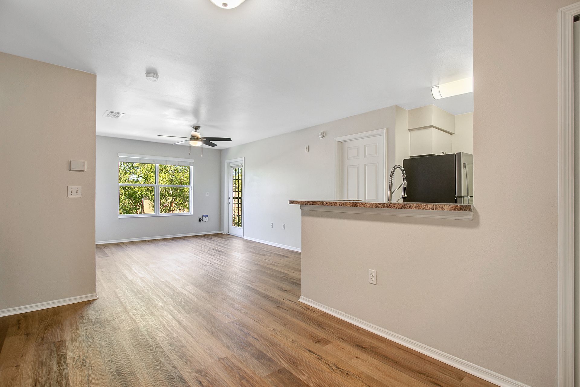 An empty living room with hardwood floors and a ceiling fan.