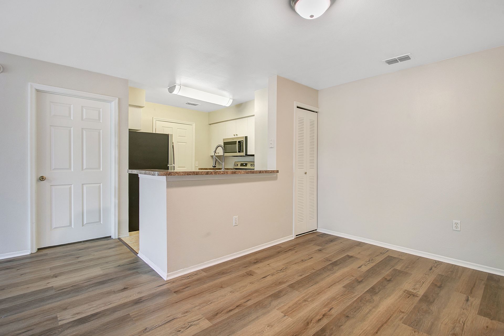A living room with hardwood floors and a kitchen in the background.