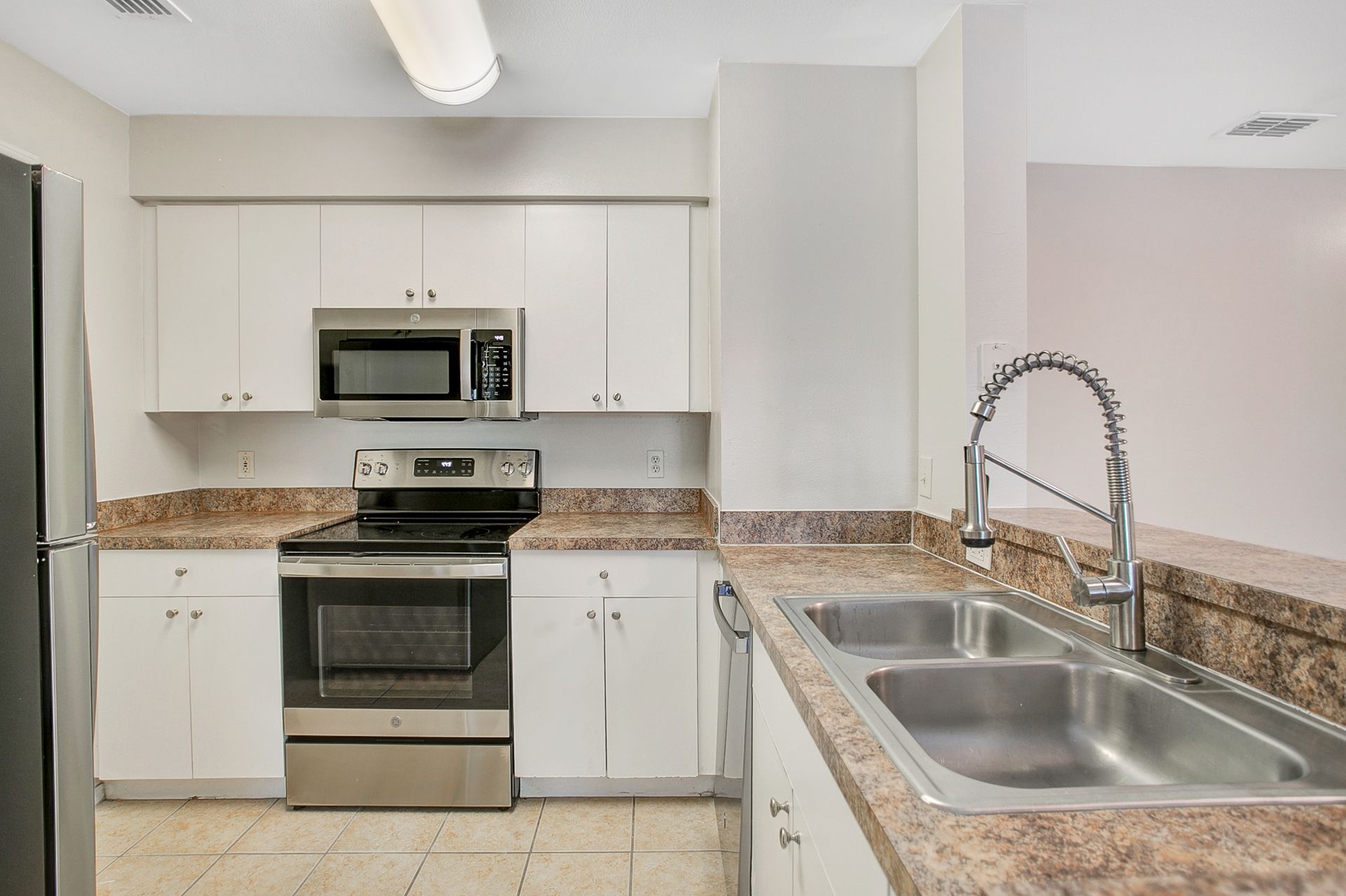 A kitchen with a sink , stove , microwave and refrigerator.