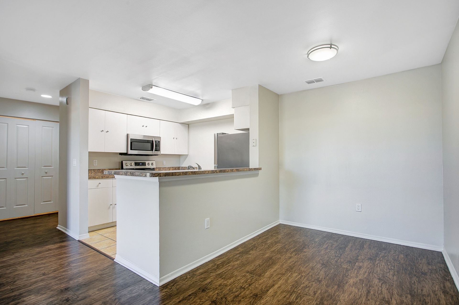 An empty apartment with a kitchen , dining room , and living room.