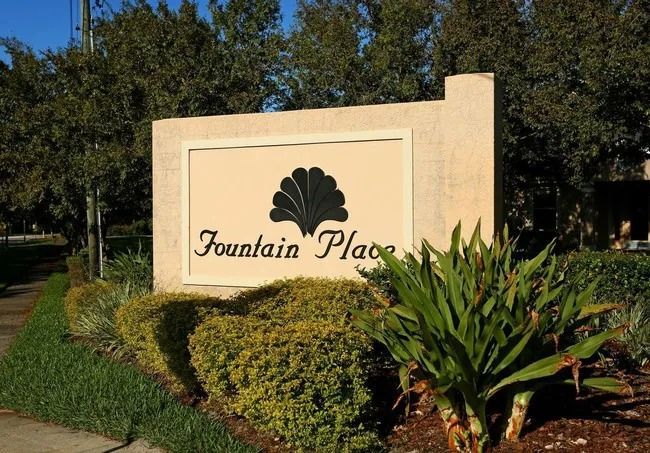 A sign for fountain place is surrounded by bushes and trees.