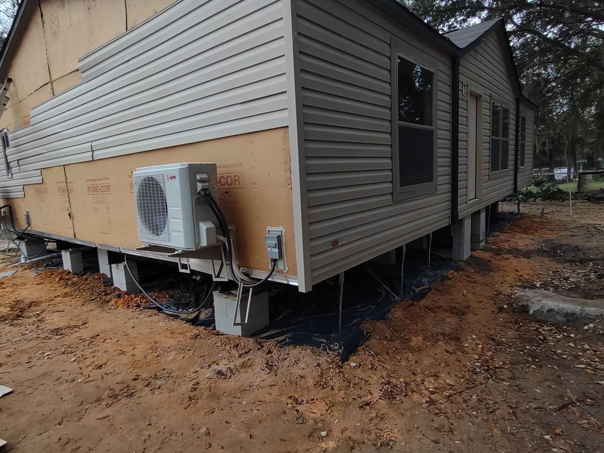 Exterior view of a manufactured home on concrete blocks with missing vinyl siding, revealing exposed insulation.