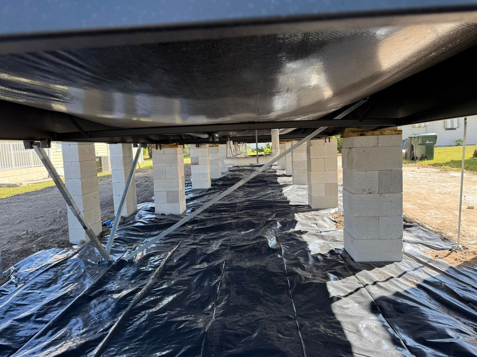 A view under a manufactured home showing concrete block piers on a ground-covering plastic vapor barrier.