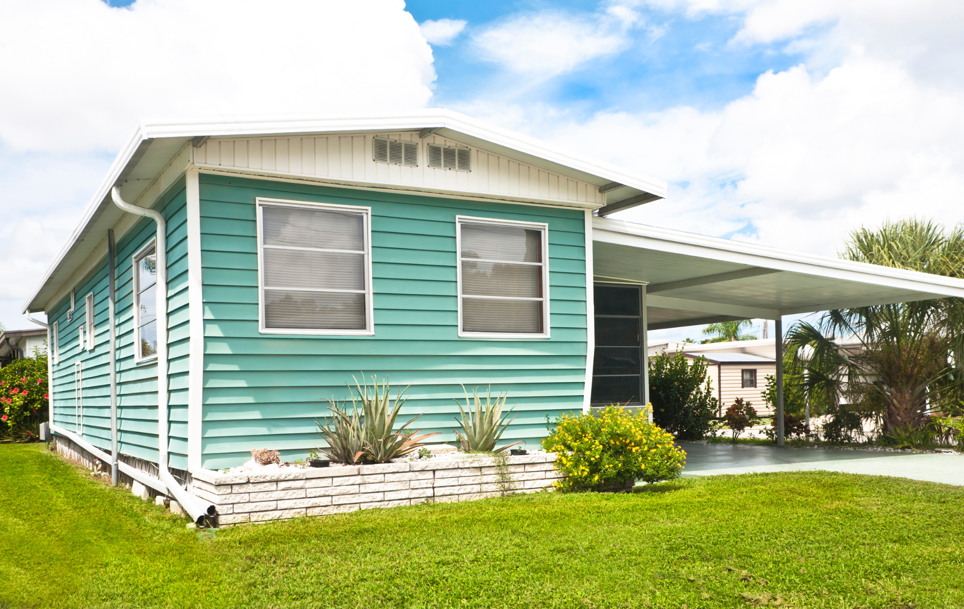 A teal single-story manufactured home with horizontal siding, two front windows, and an attached white carport.