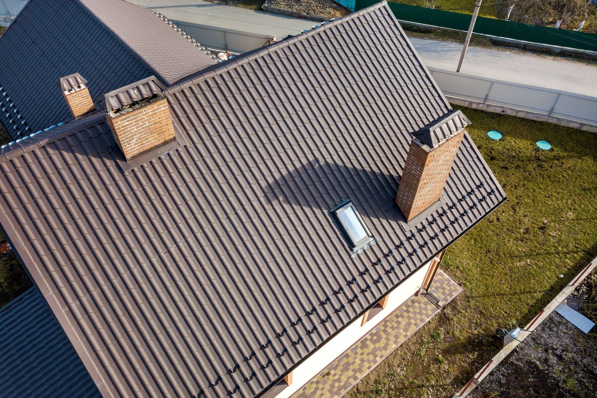 Aerial view of a gray-tiled house roof with two brick chimneys and a skylight.