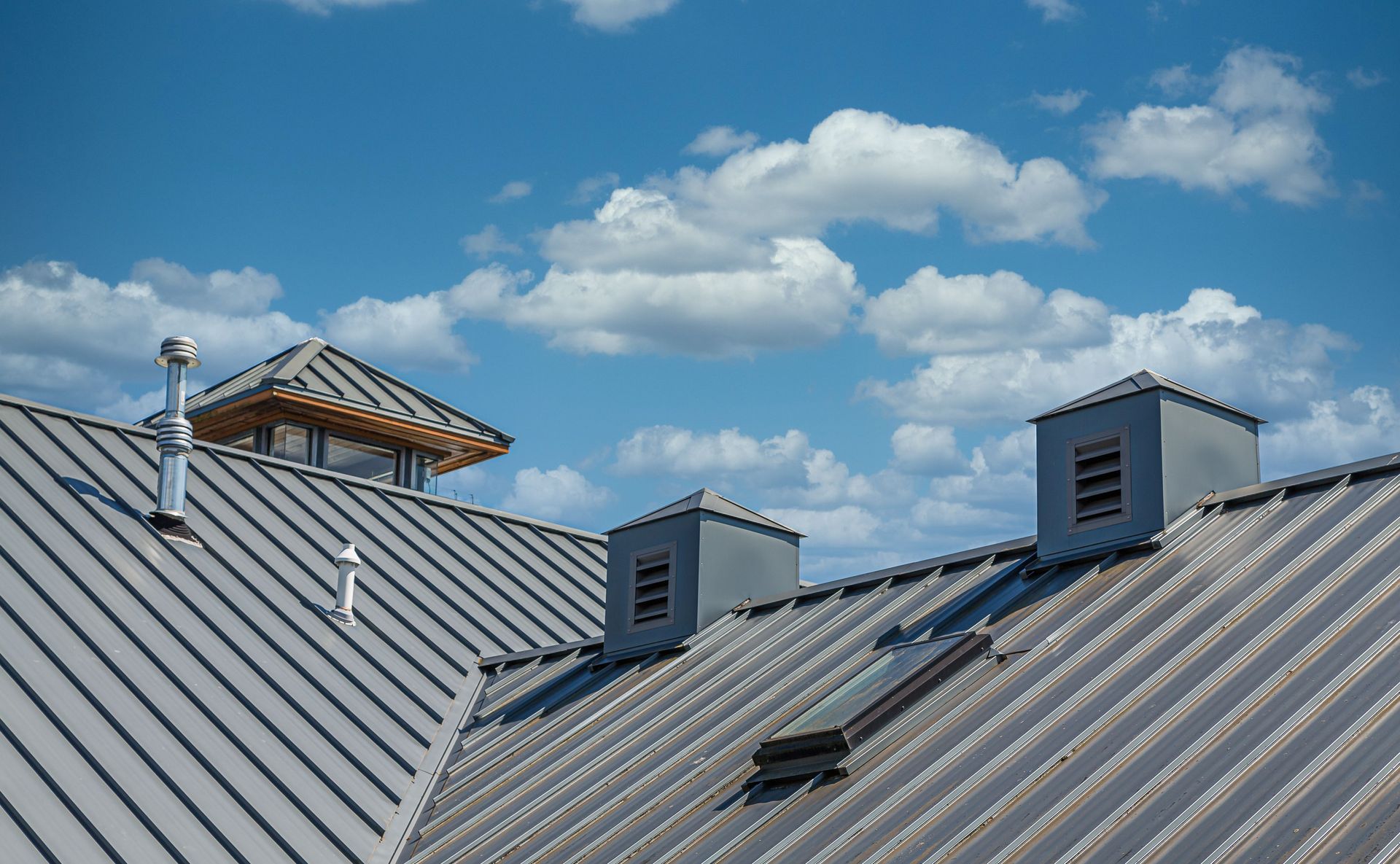 Metal rooftop with skylights and a wooden roof structure under a blue sky with scattered clouds
