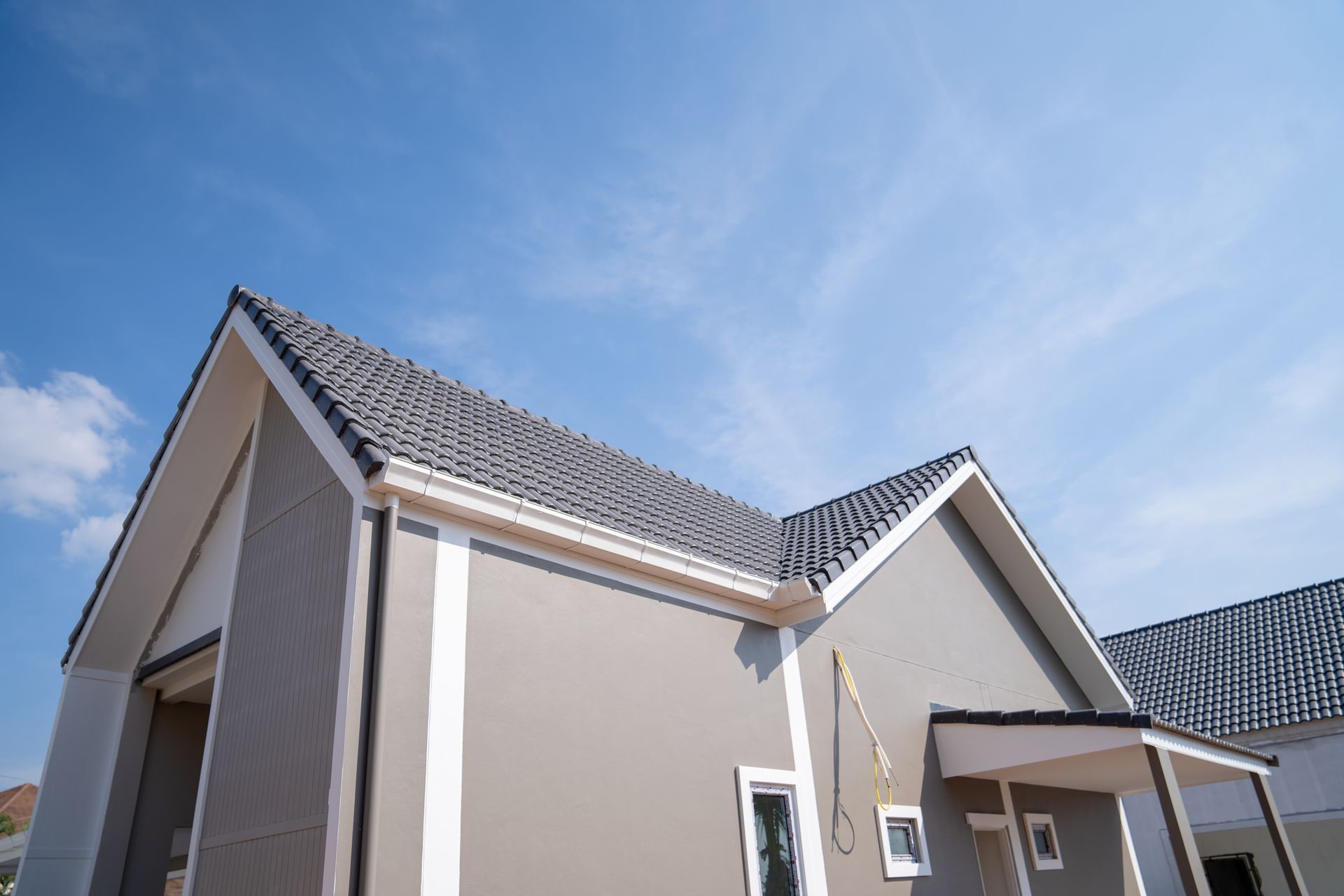 Gray and white house with dark roof against a blue sky.