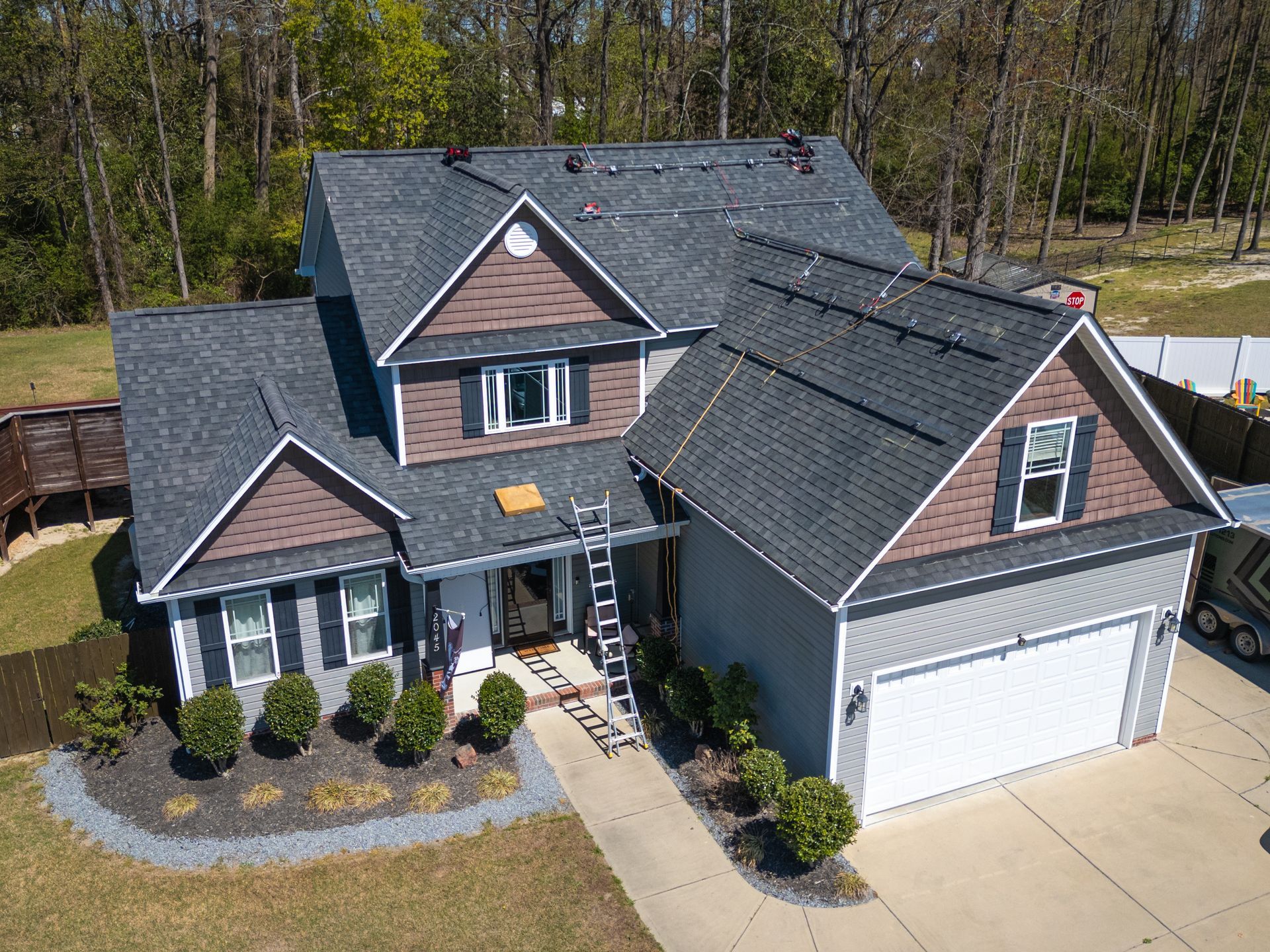 Aerial view of a gray house with a brown trim, a ladder, and trees in the background.